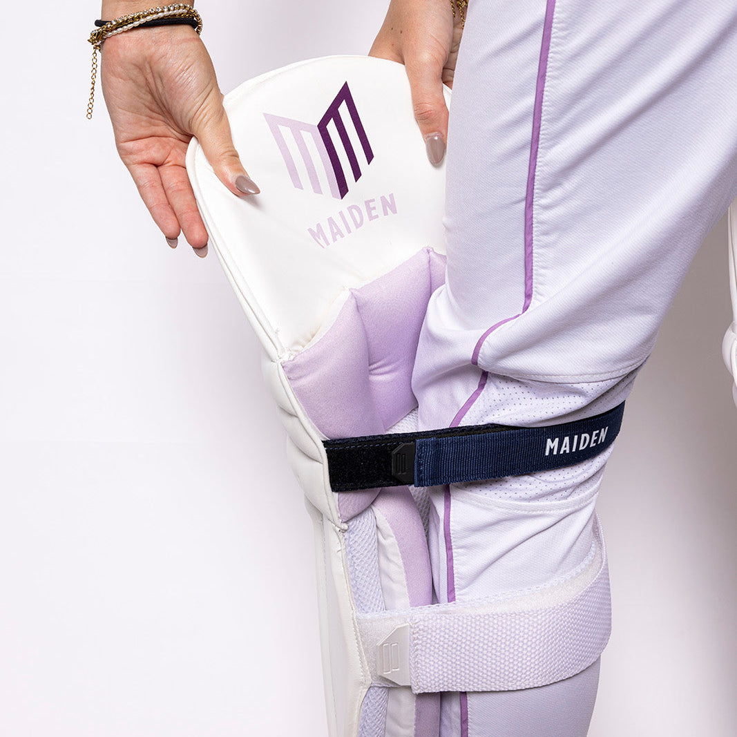 Person wearing a white outfit with purple accents, holding a white box with 'MAIDEN' branding.