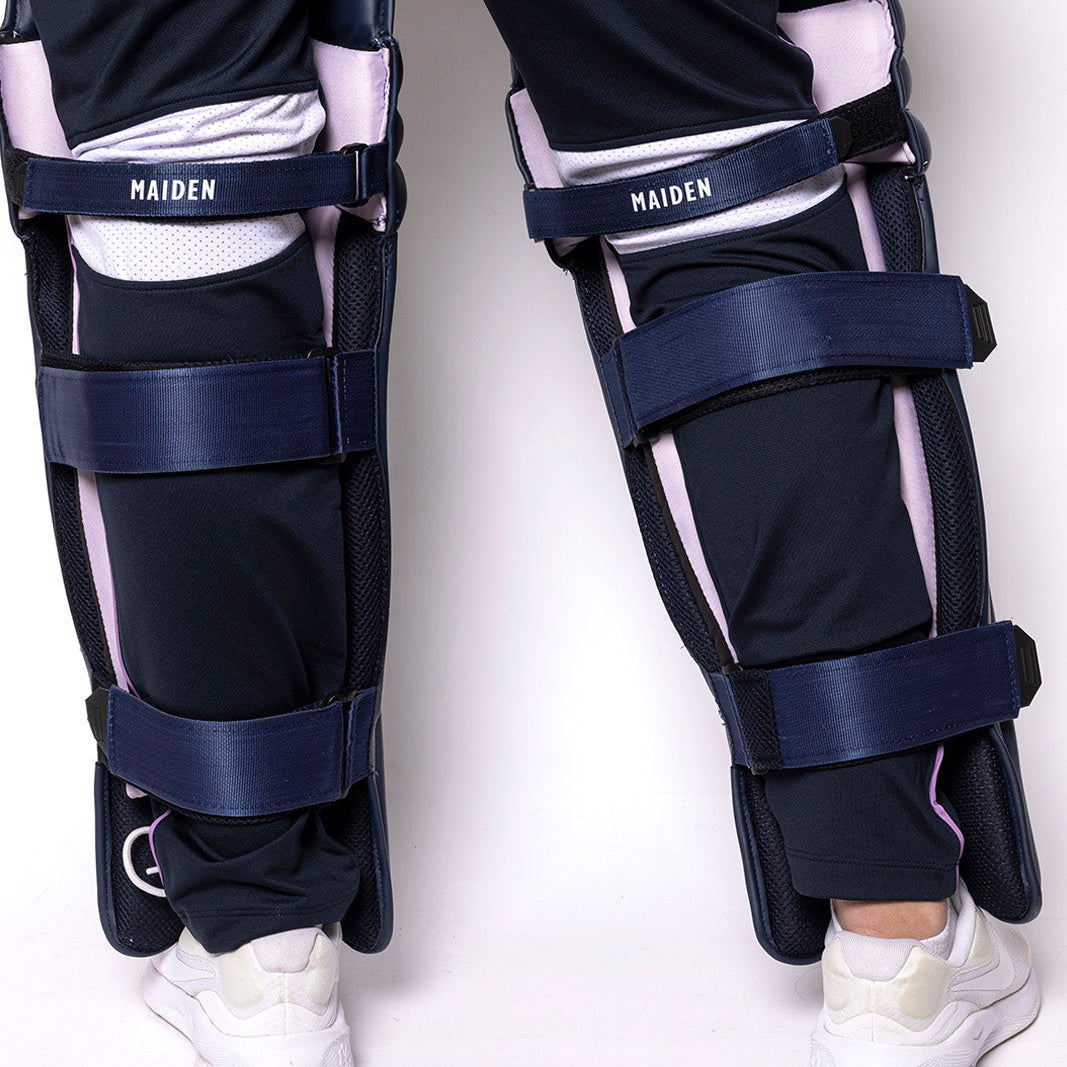 Navy leg guards with white accents on a person wearing black pants and white shoes against a white background.