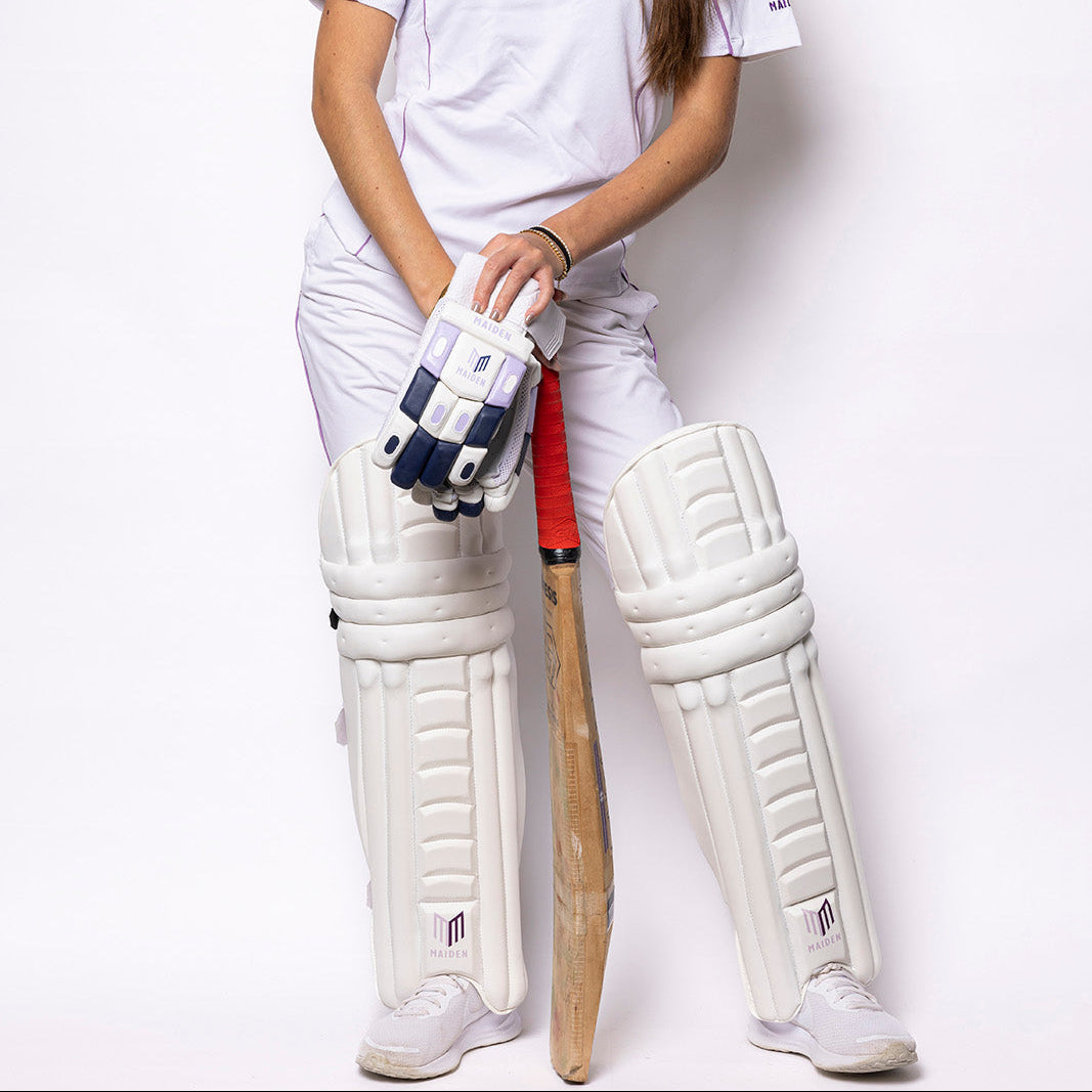 Person wearing a cricket uniform with a bat and gloves on a white background