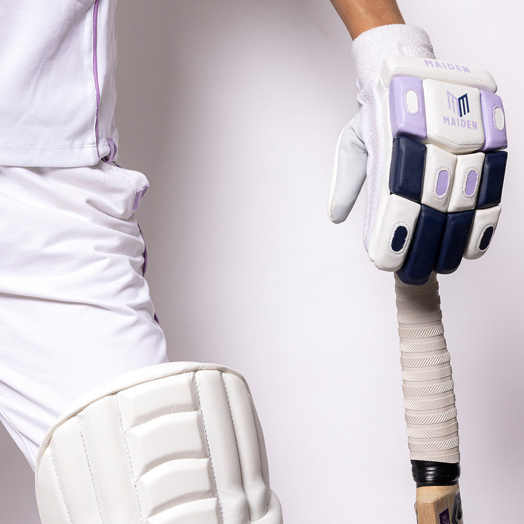 Person wearing white cricket gear with a bat and protective pads on a plain background