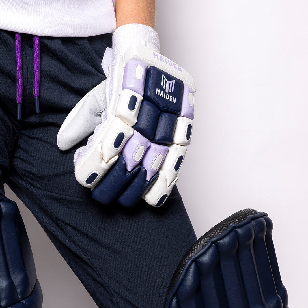 Person wearing white batting gloves with black accents and a visible brand logo, holding a black protective pad.