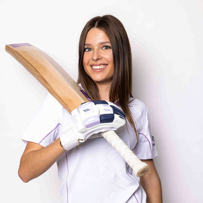 Woman in cricket gear holding a bat against a white background