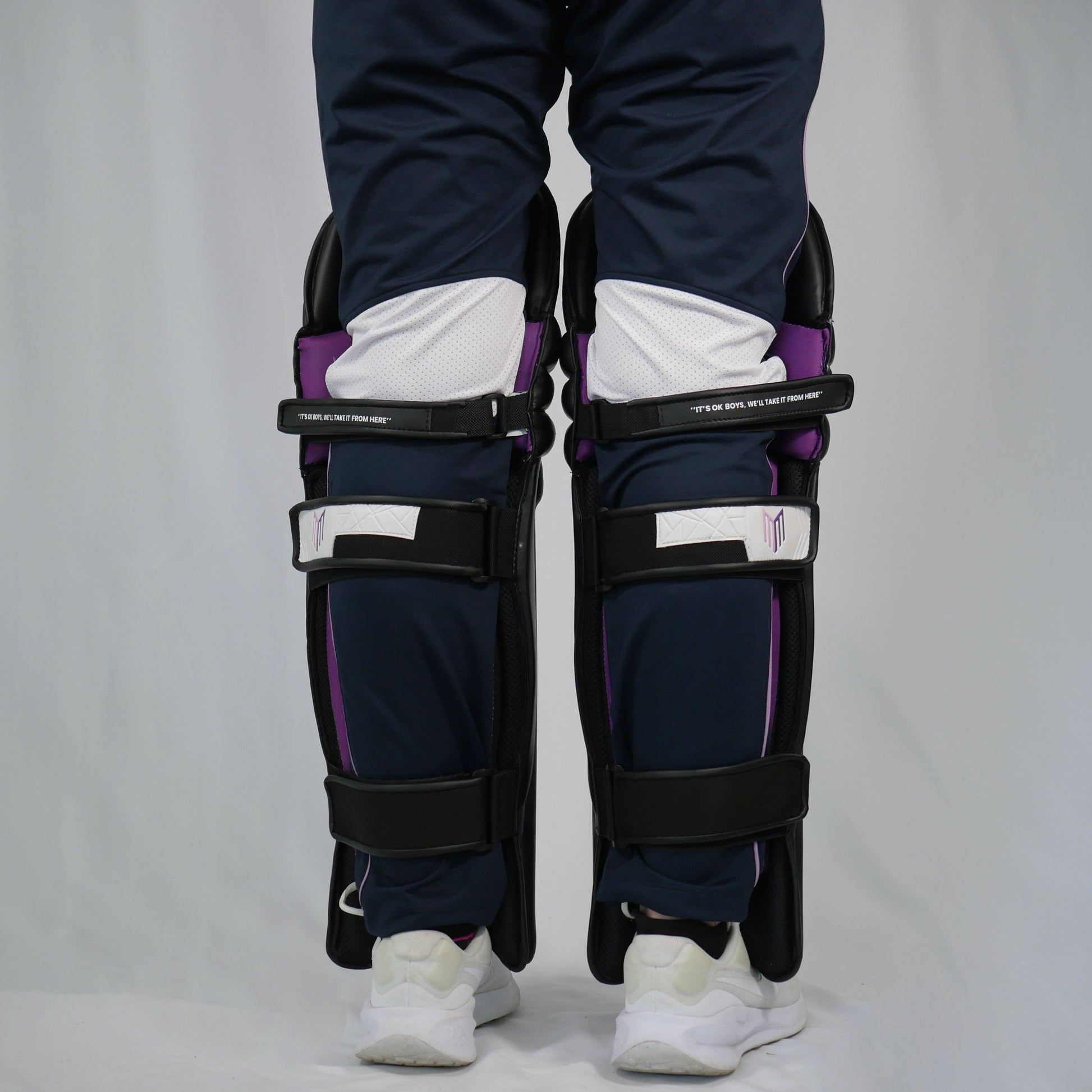 Person wearing black shin guards with purple accents on a plain background