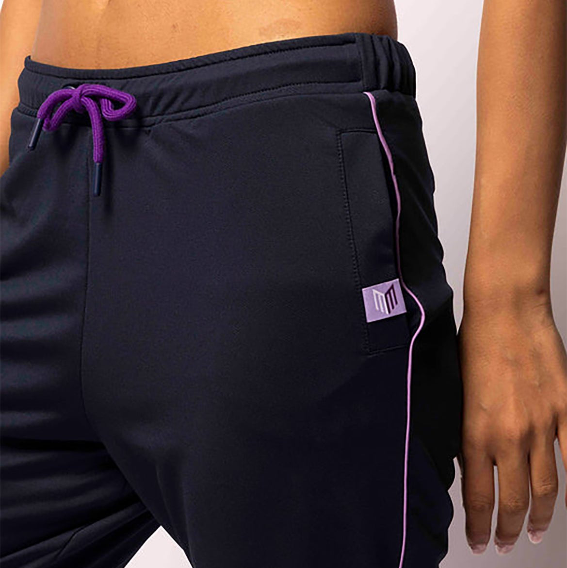 Black athletic pants with purple drawstring and trim on a plain background