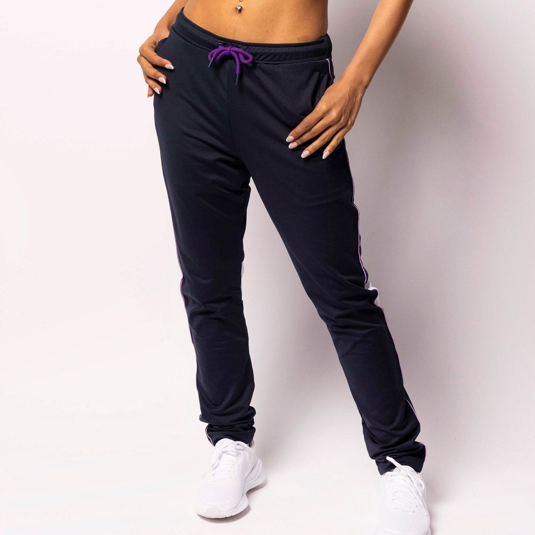 Person wearing a black sports bra and navy jogger pants with white sneakers on a light background