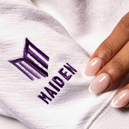 White garment with 'MAIDEN' logo embroidered on it, hand touching fabric