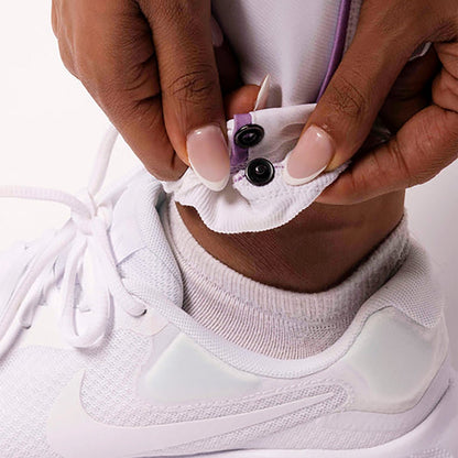 Person adjusting a white athletic shoe with a sock on a light background